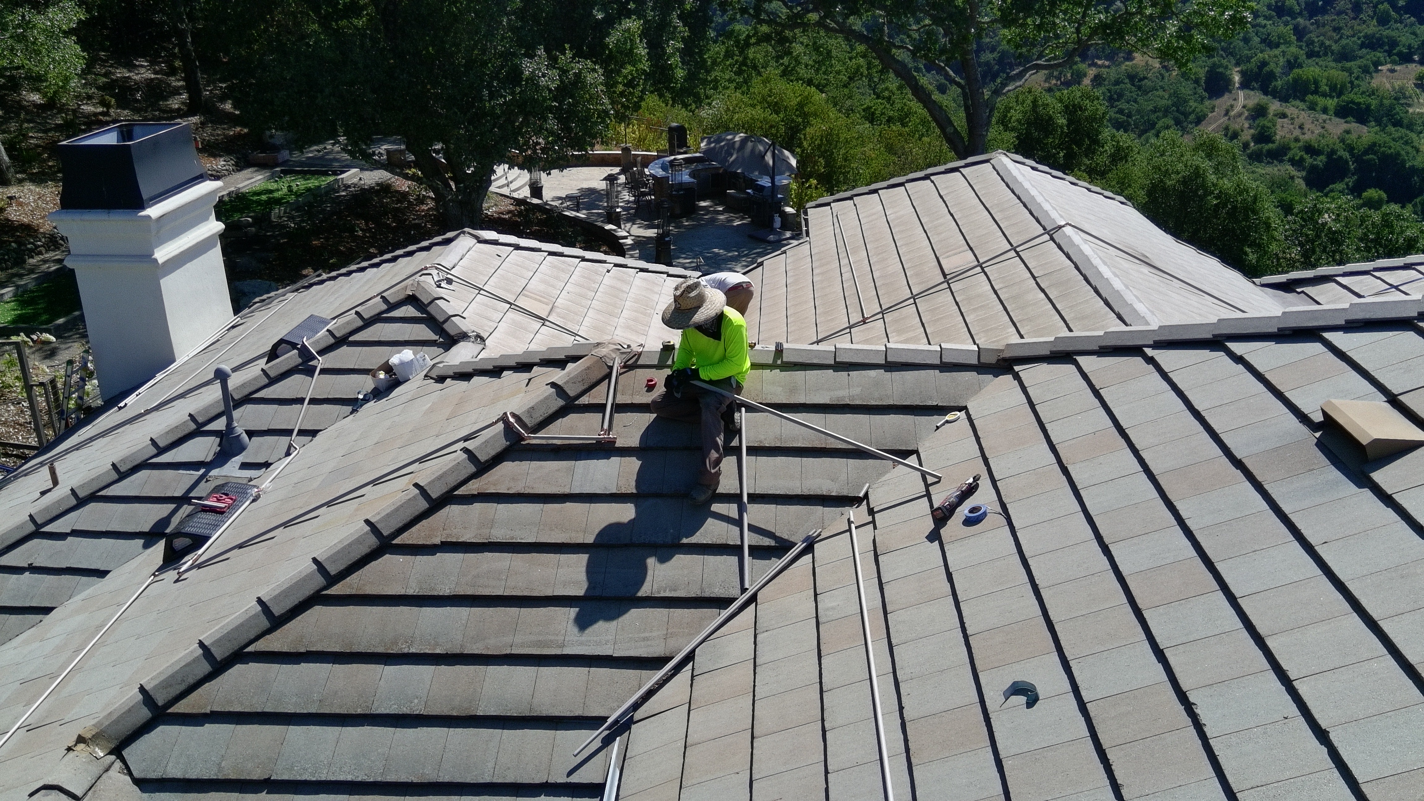 FireRoofs technician routing copper pipe along roof ridgeline with hillside views