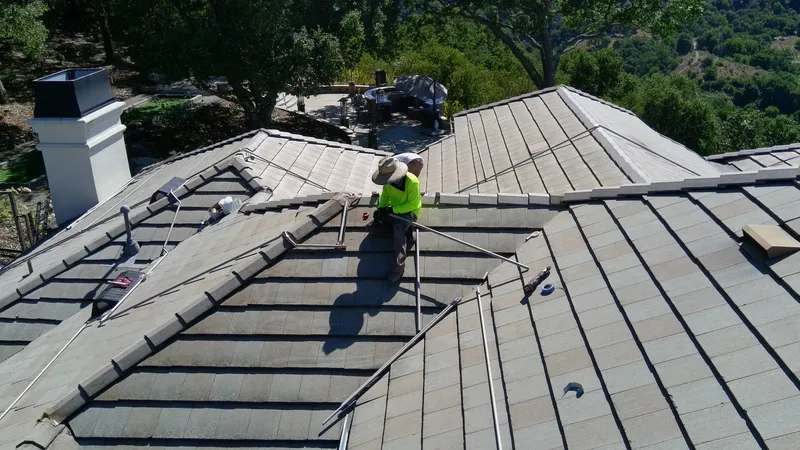 FireRoofs technician routing copper pipe along roof ridgeline with hillside views