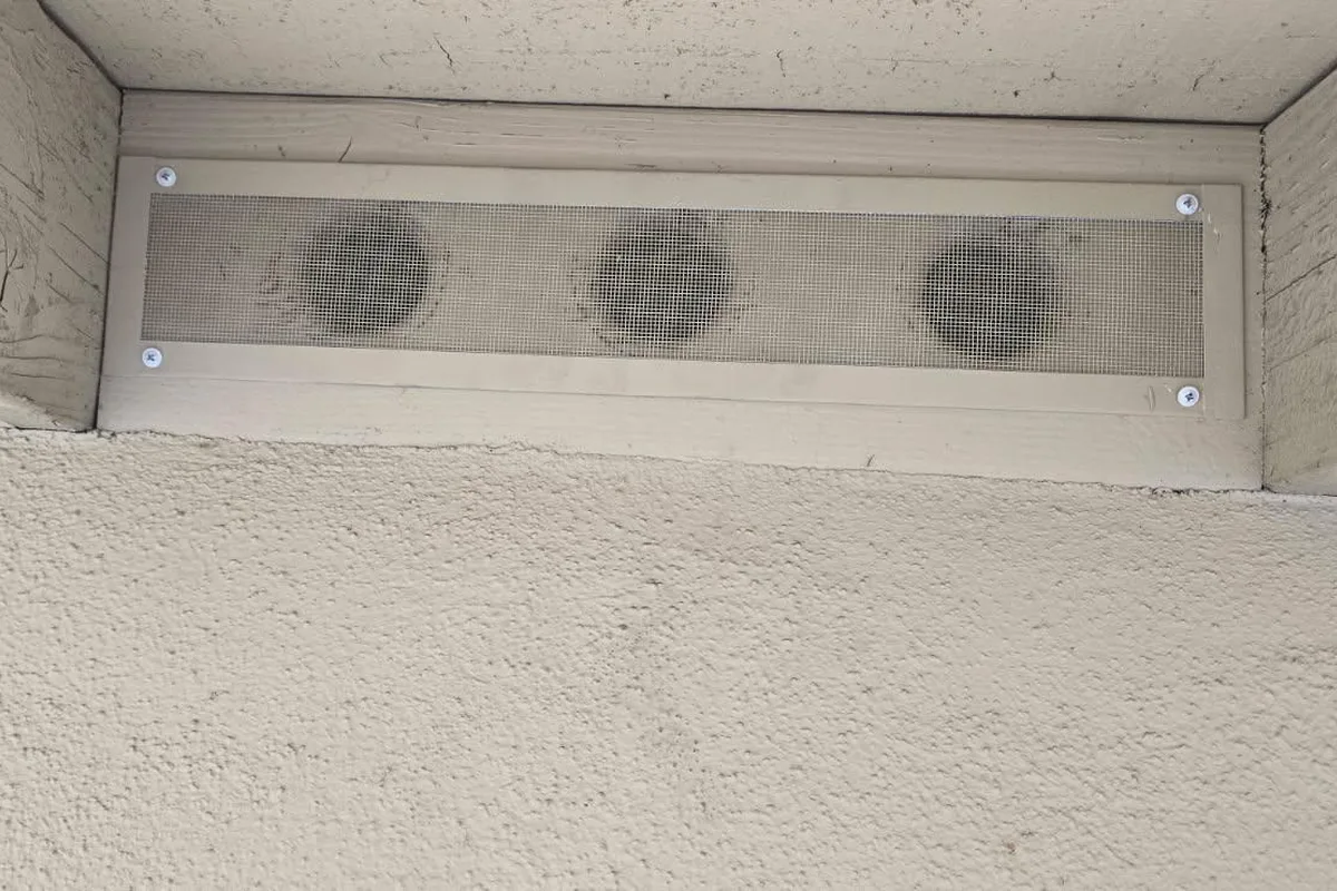 Three-port eave vent retrofitted with an ember-resistant fine mesh cover screwed over the original openings