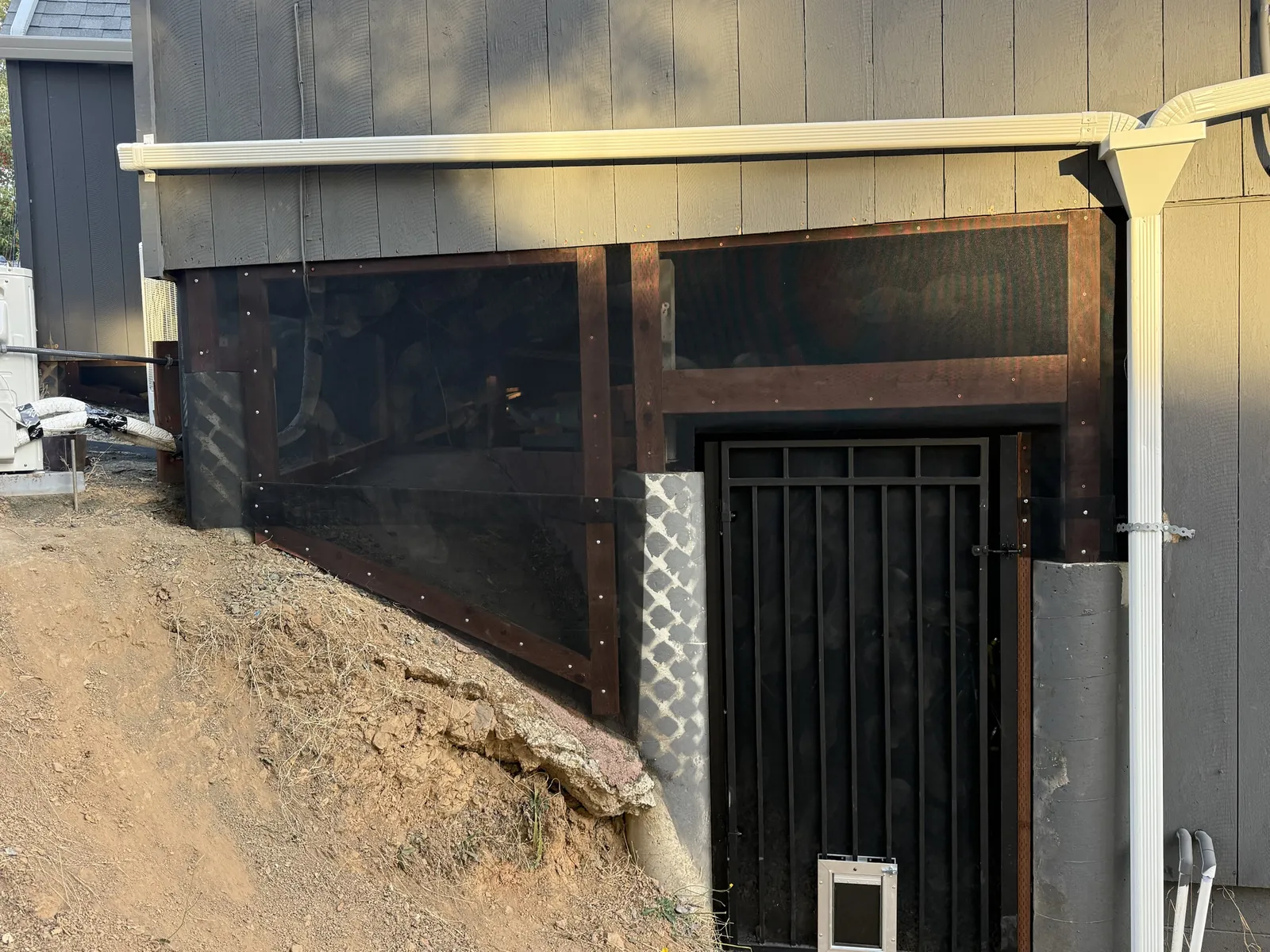 Hillside home with the open space under the house enclosed in new 1/16-inch ember and flame resistant mesh and a new black metal gate