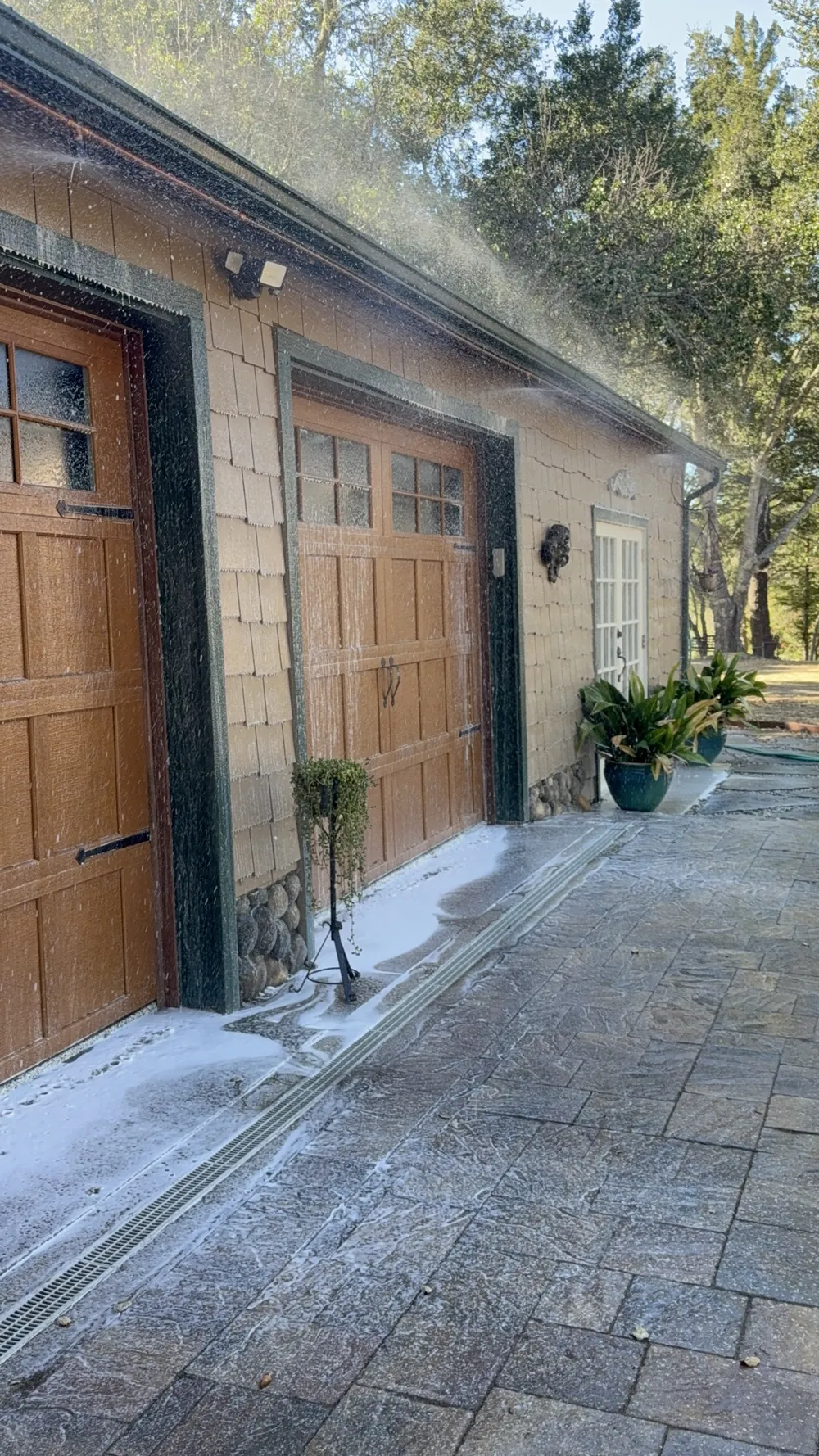 Eave sprinklers spraying a Class A foam and water mix over garage doors, siding and the driveway of a hillside home