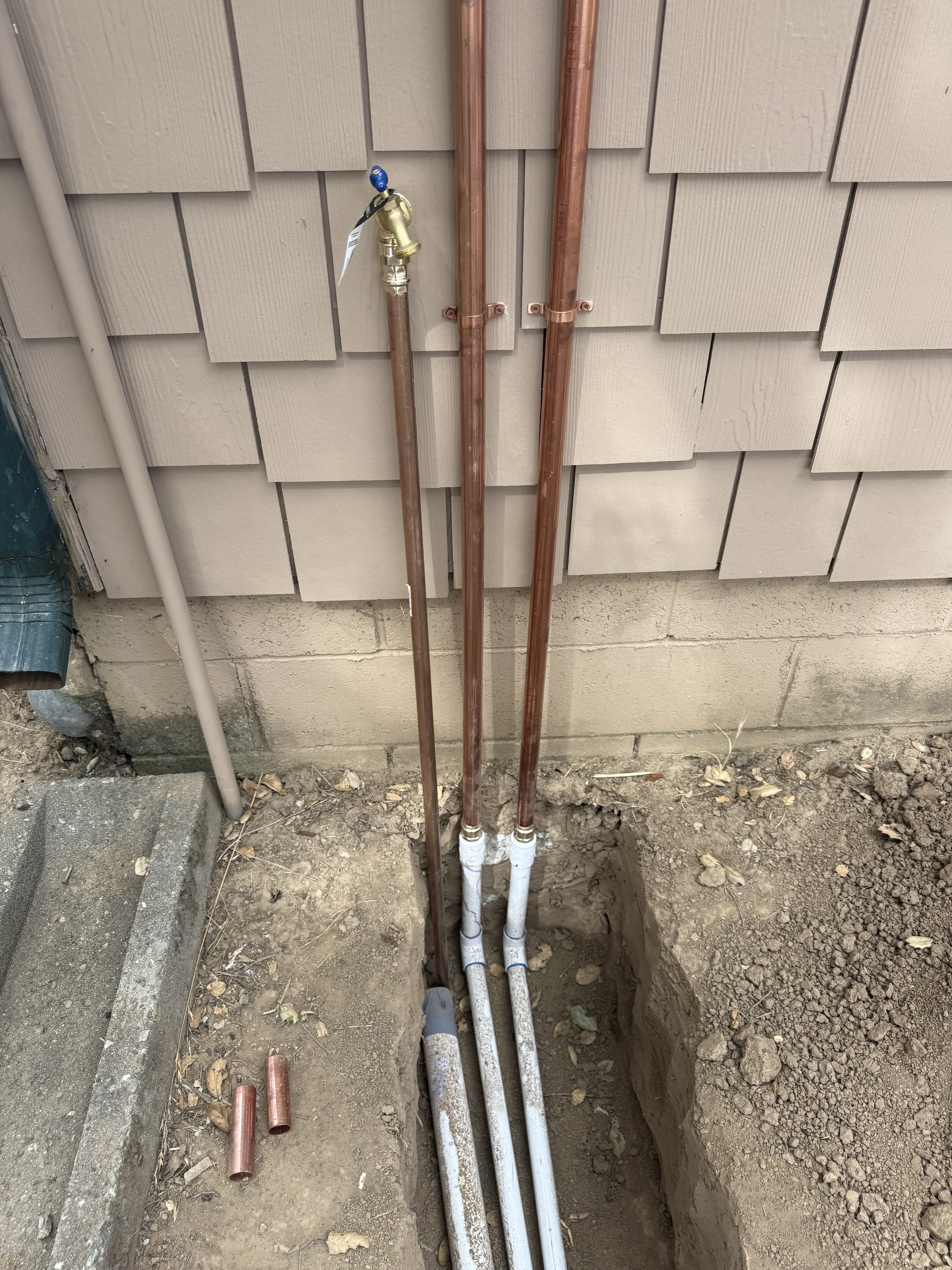Three copper risers with a brass shutoff valve emerging from underground supply lines at the foundation of the Summit Road home