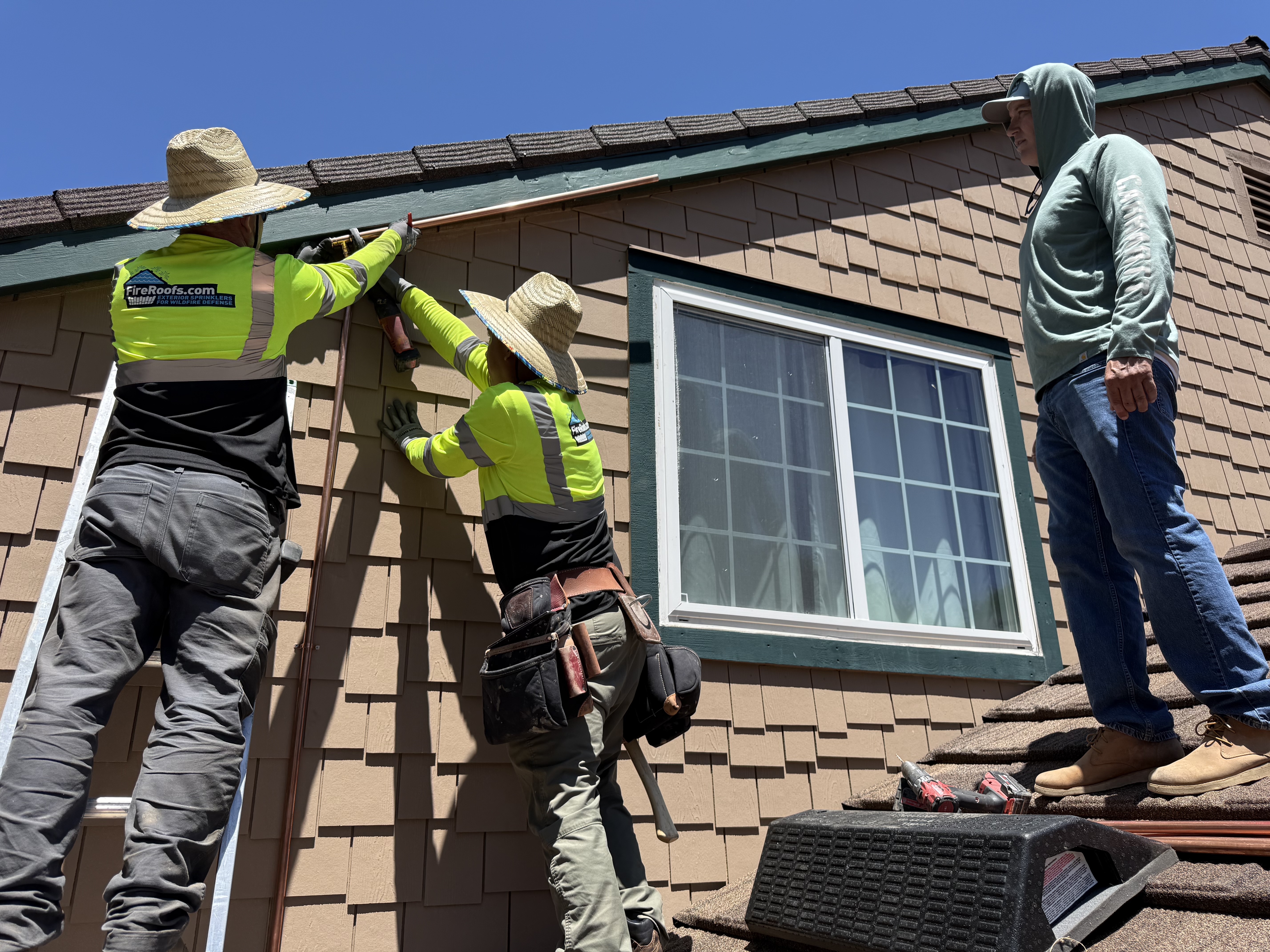 FireRoofs crew in high-visibility vests installing copper sprinkler lines along the roofline of a home off Summit Road in the Santa Cruz Mountains