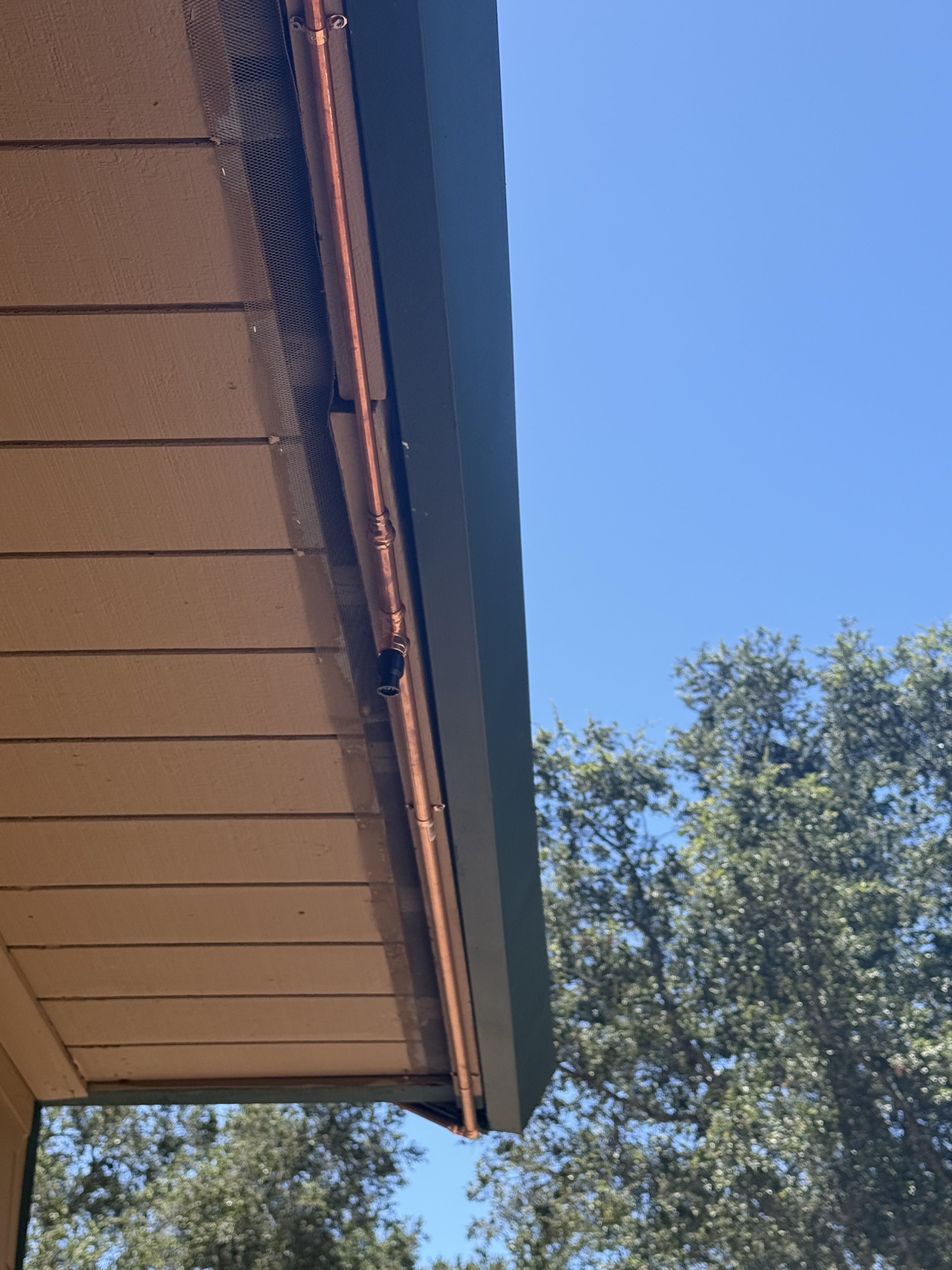 Copper supply line running along the soffit with a sprinkler nozzle at the roofline edge of the Summit Road home