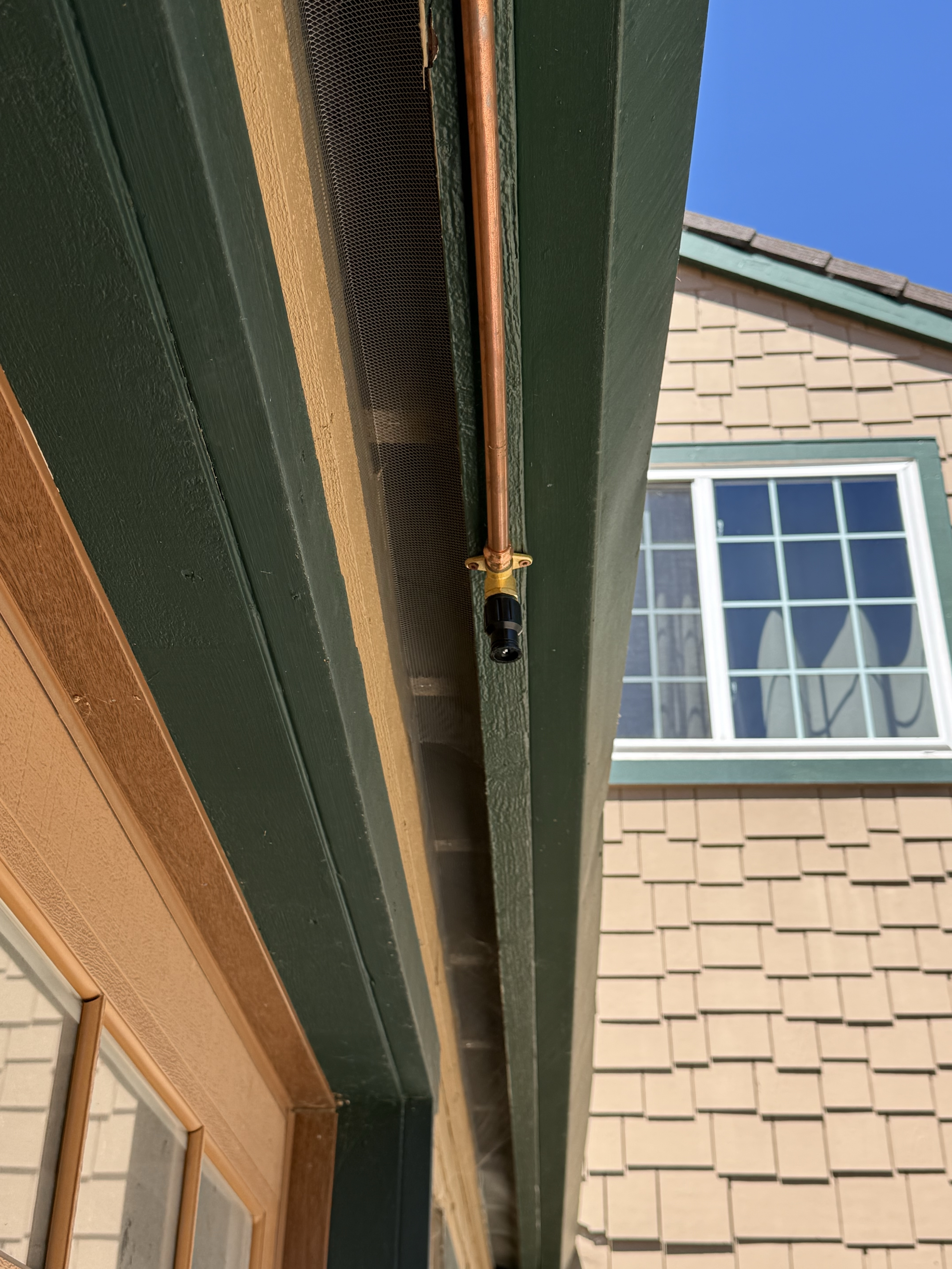 Close-up of a copper sprinkler line and nozzle tucked between green fascia boards at the Summit Road property eave line