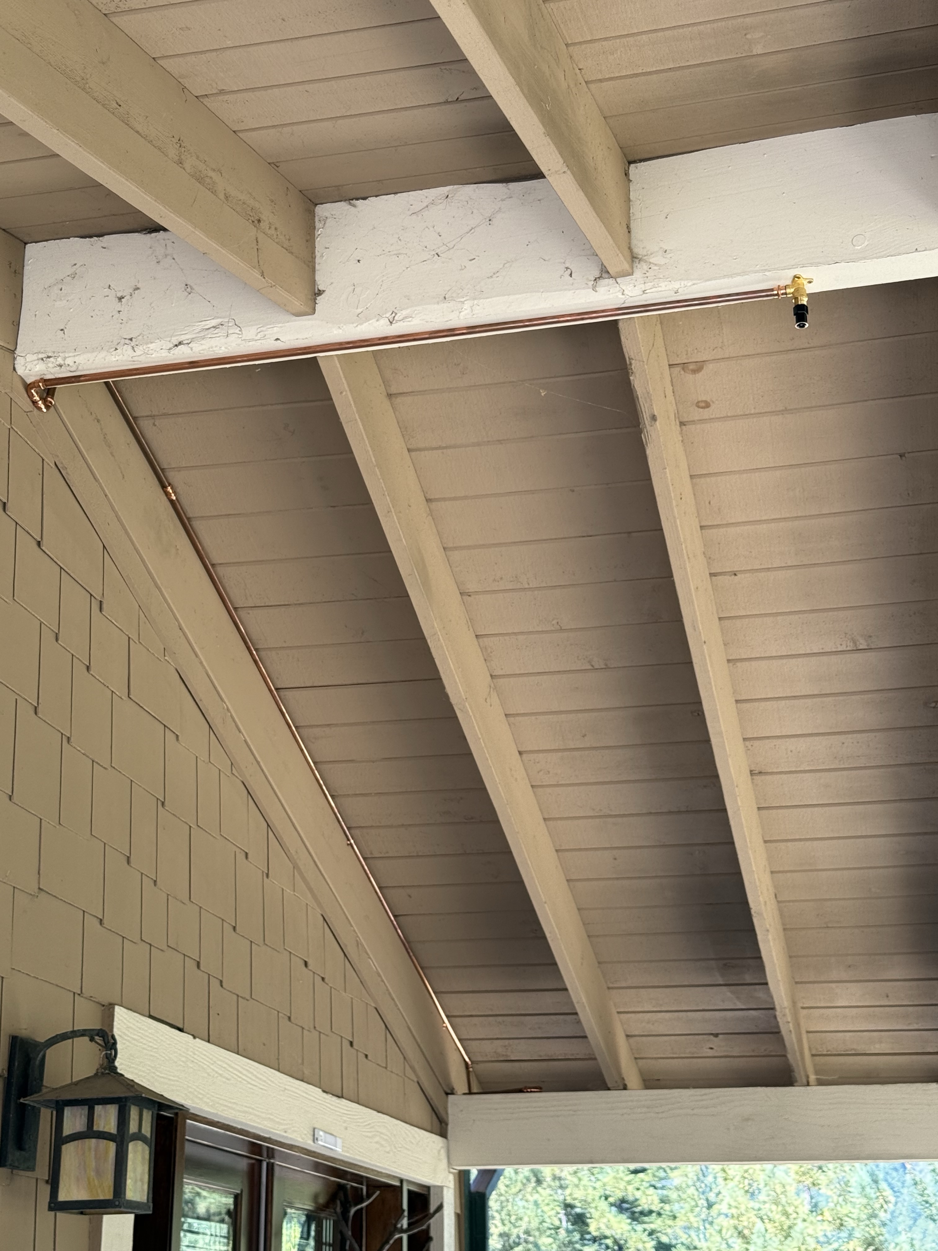 Copper sprinkler line with a nozzle mounted under a covered porch ceiling at the Summit Road property in the Santa Cruz Mountains