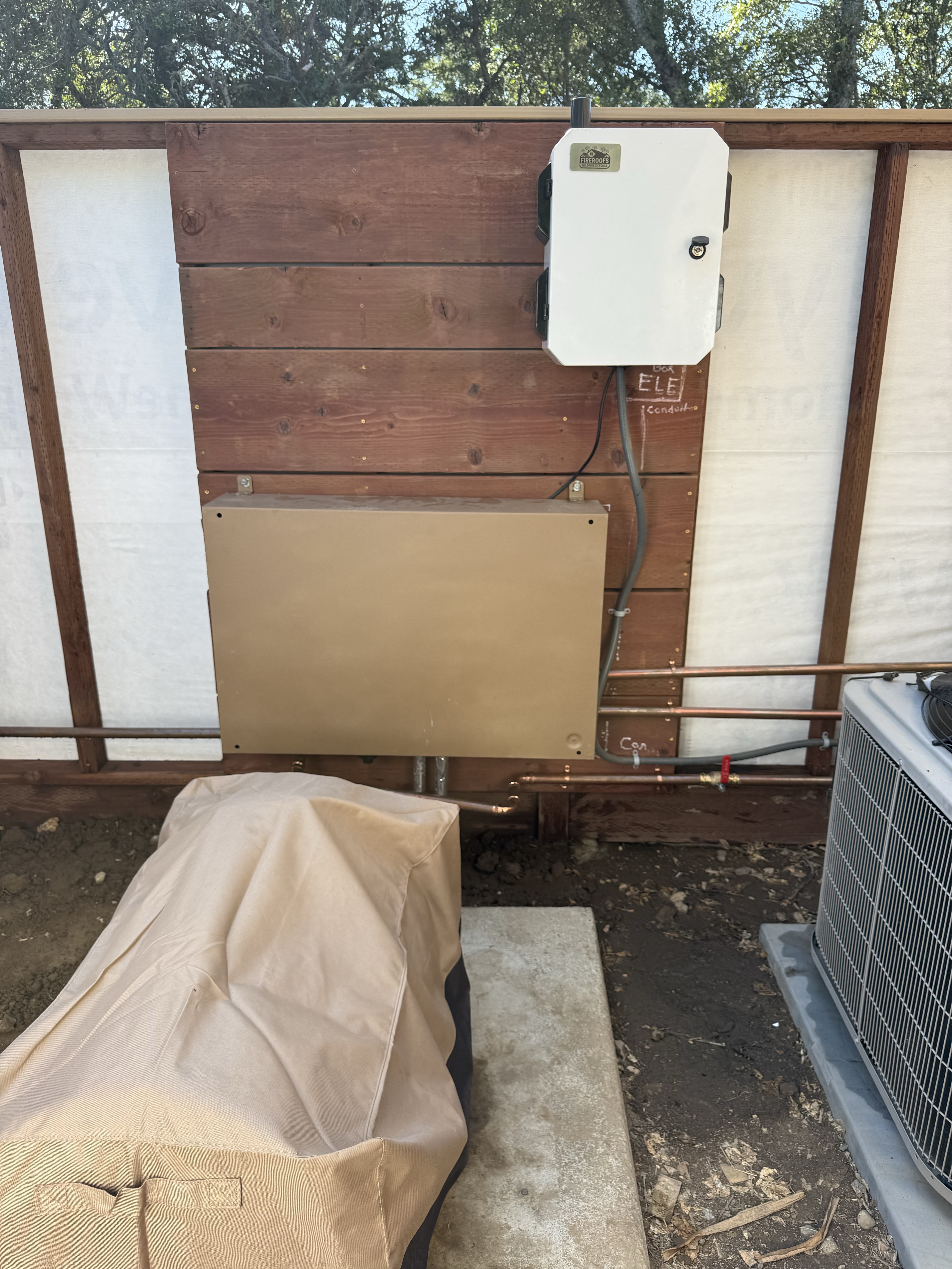 FireRoofs smart controller mounted on the exterior wall next to the electrical panel at the Summit Road property, with copper supply lines leading to the sprinkler system