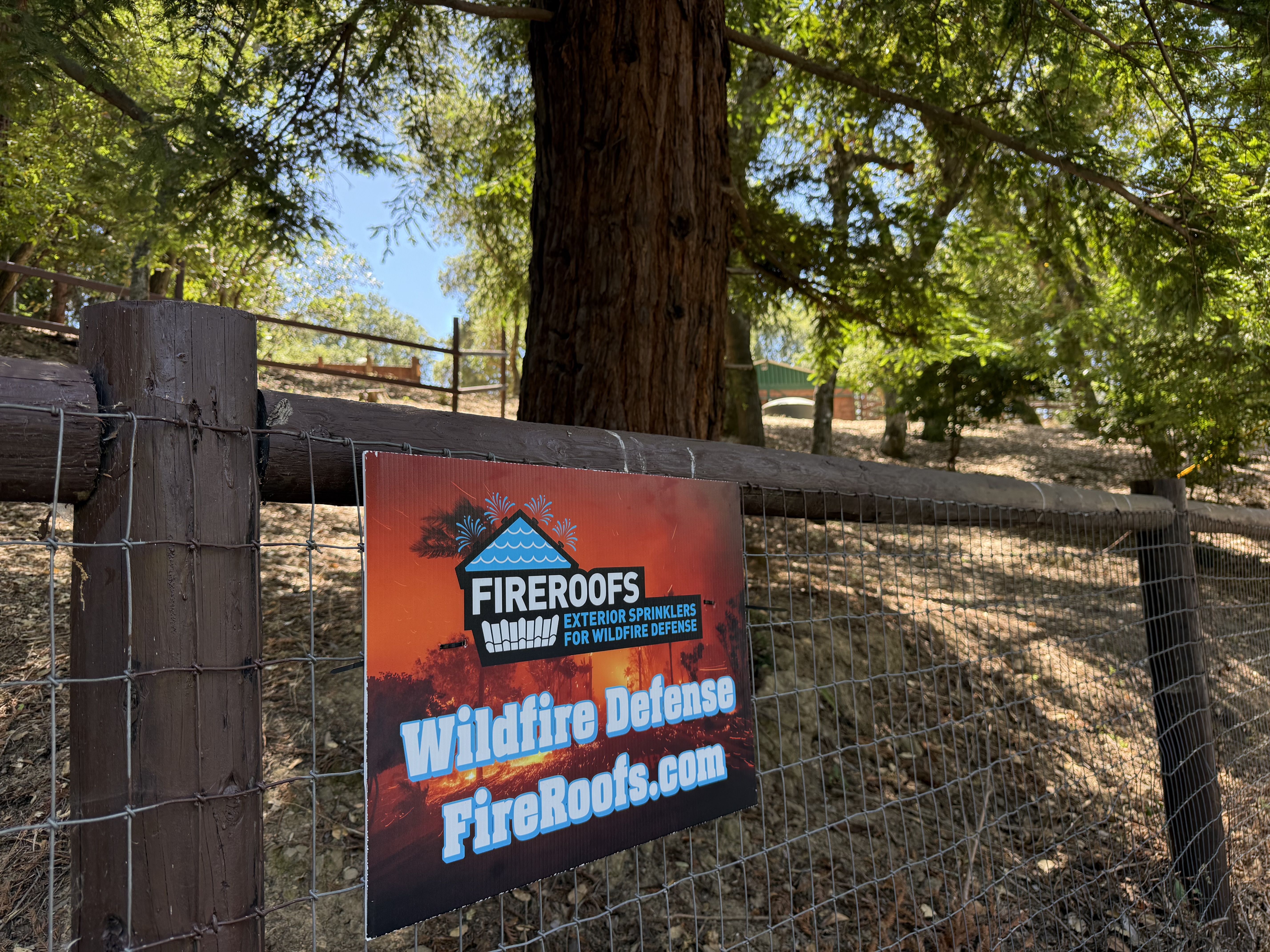 FireRoofs Wildfire Defense yard sign on a fence at a wooded property off Summit Road in the Santa Cruz Mountains