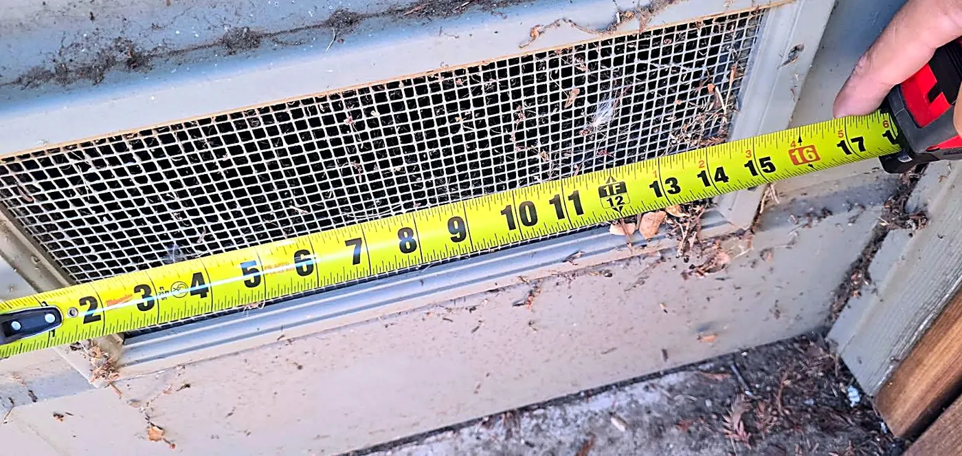 Crawlspace vent with an old quarter-inch screen measured with a tape measure