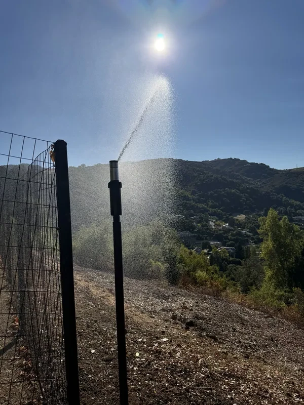 FireRoofs perimeter wildfire sprinkler spraying water across hillside vegetation