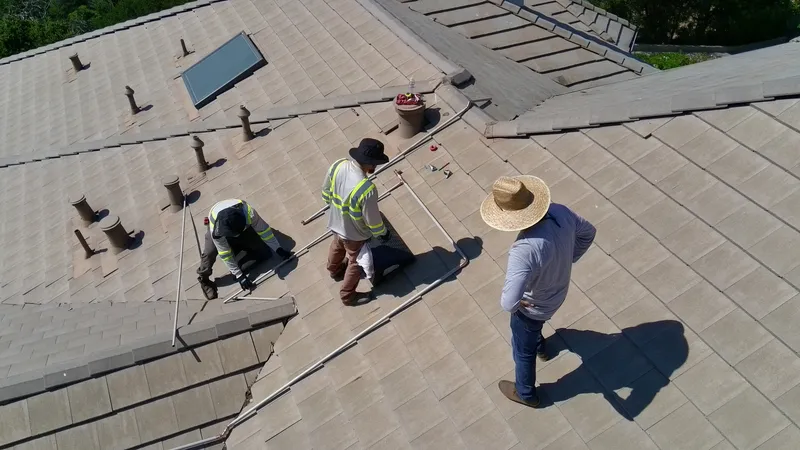 FireRoofs installation crew fitting copper sprinkler pipes along a tile roof ridge on a Bay Area home