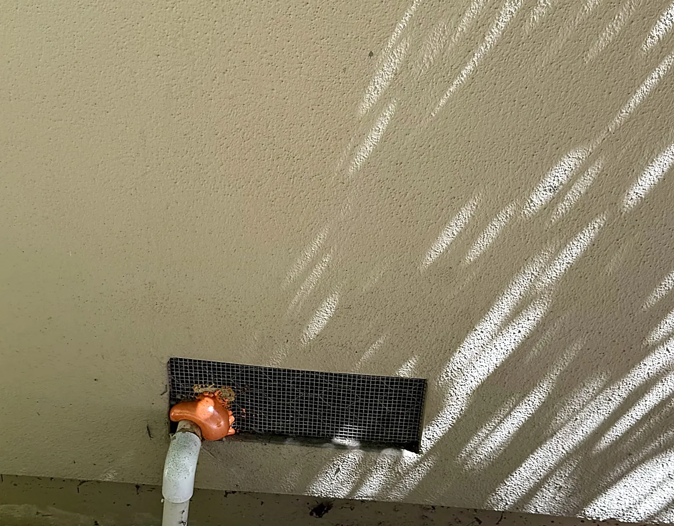 Foundation vent covered with ember-resistant mesh and sealed around a pipe with fire-block foam