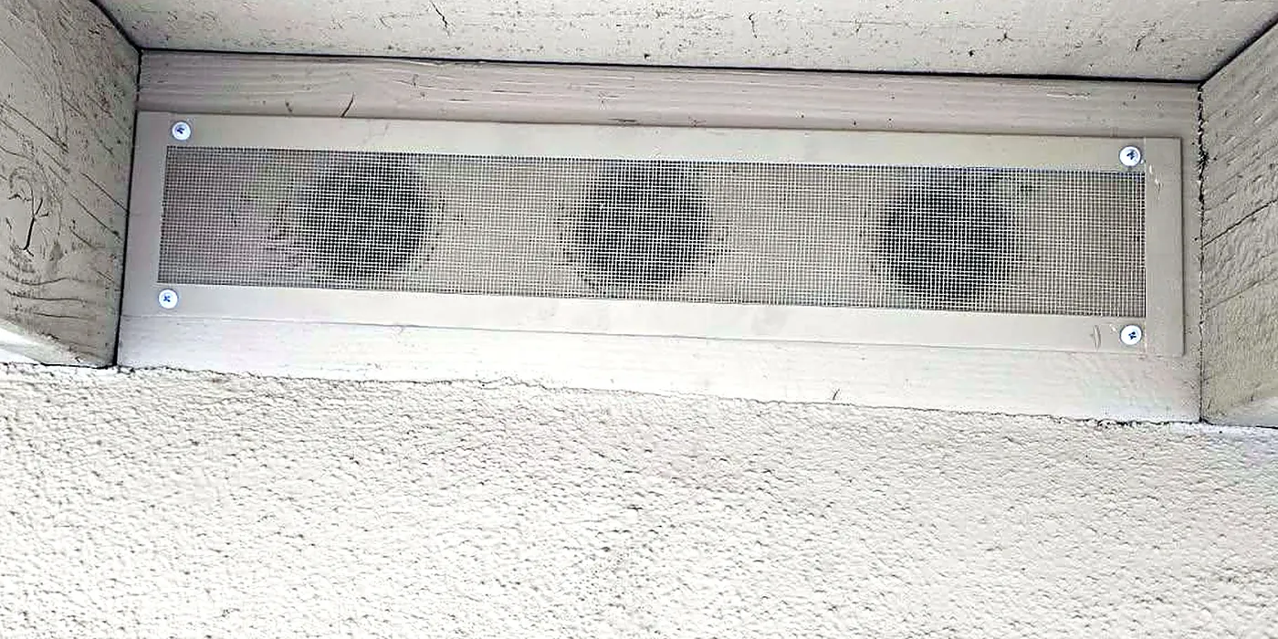 Close-up of a soffit vent covered with a fine metal mesh ember screen