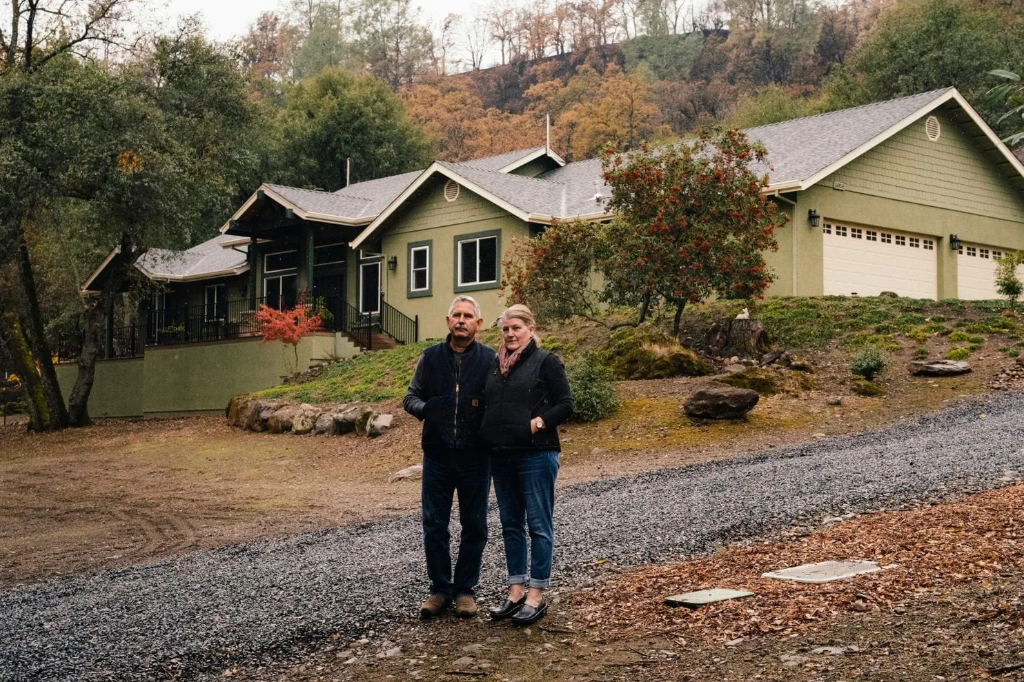 Cathy and Jeff Moore stand in front of their home in Chico, California after the 2018 Camp Fire, with exterior sprinklers visible on the roof