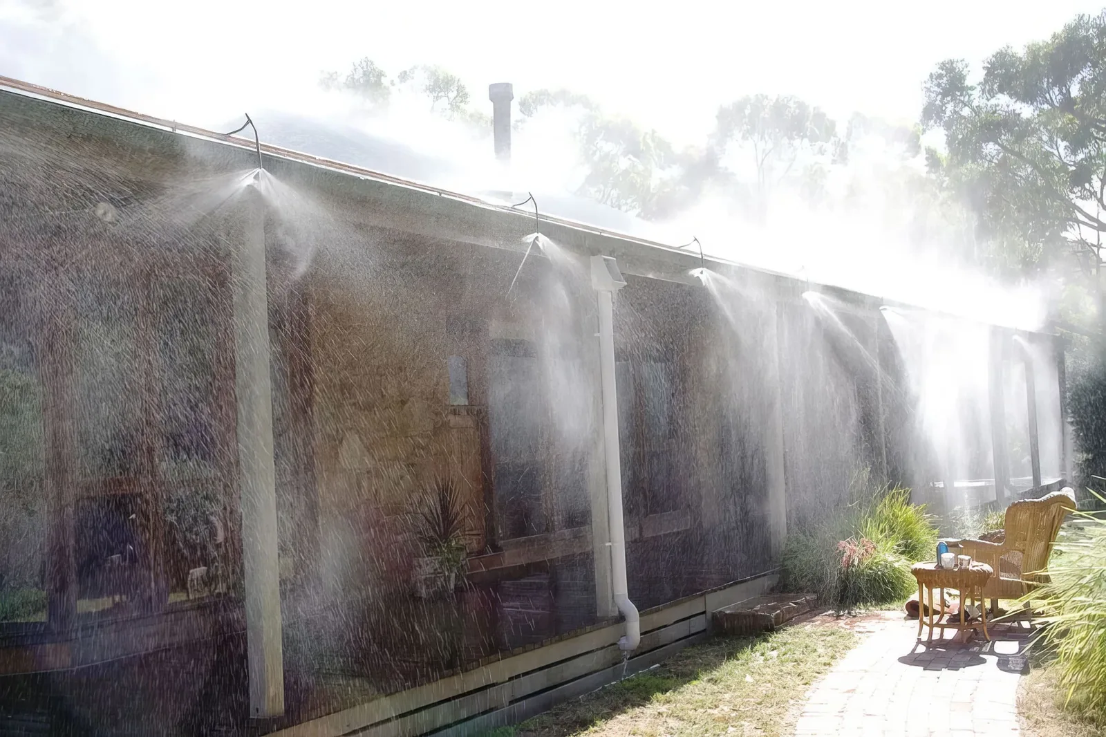 Roof-mounted exterior sprinklers actively spraying water to protect a home during wildfire conditions with smoke visible in the background