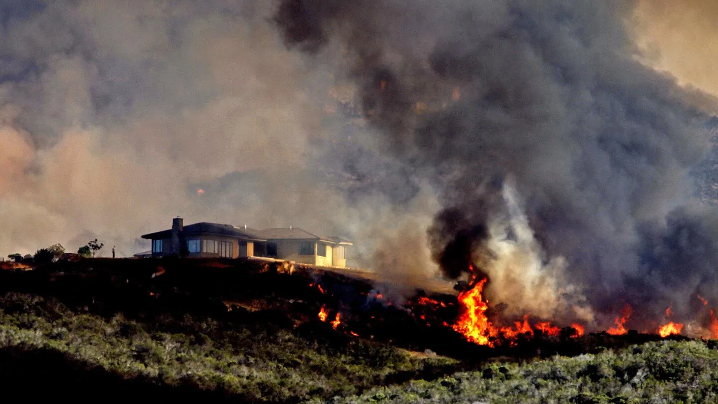 Wildfire flames burning on a hillside at night approaching residential homes in a California WUI neighborhood