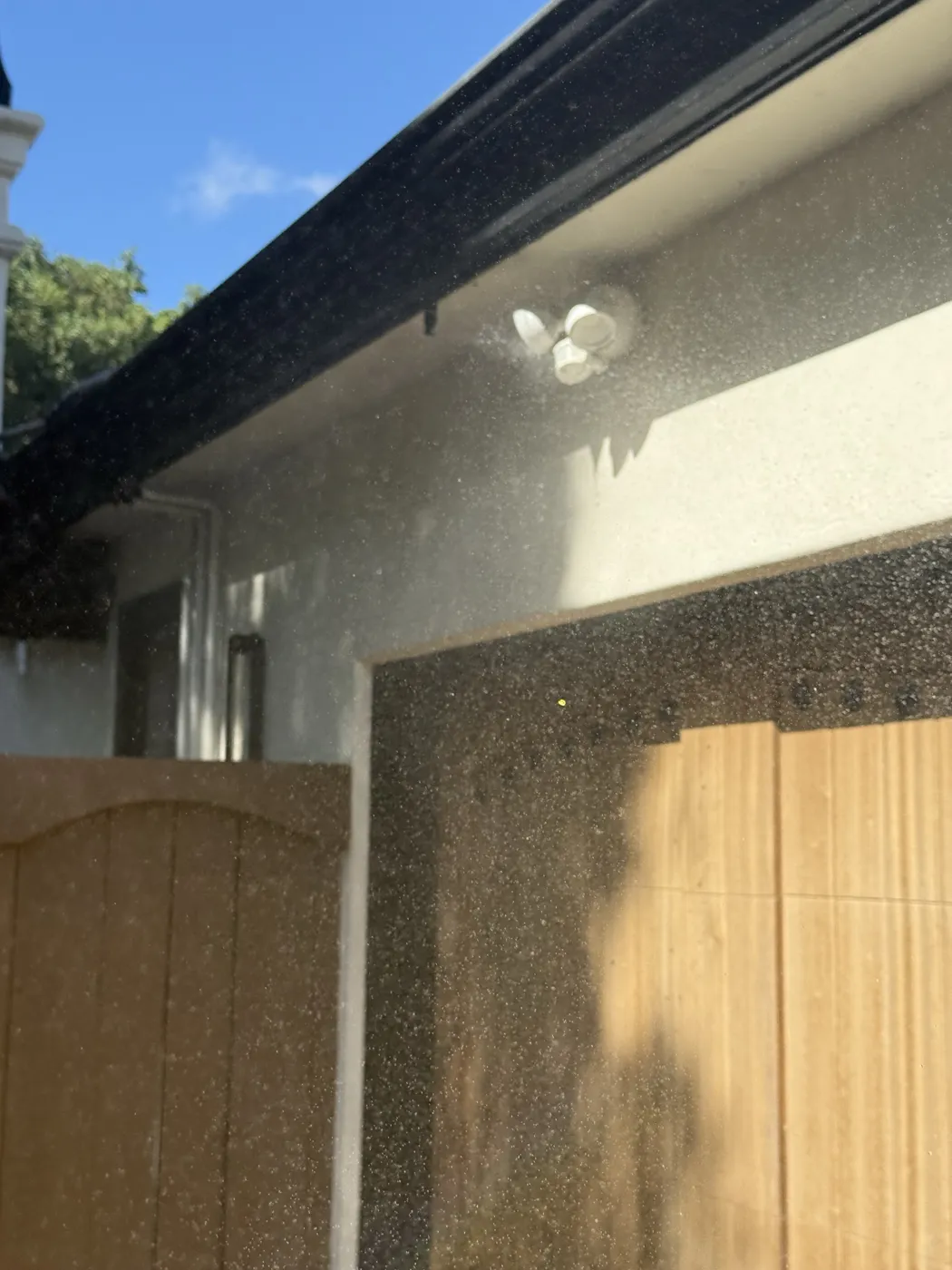 Eave sprinkler misting the wall and garage door of a stucco home