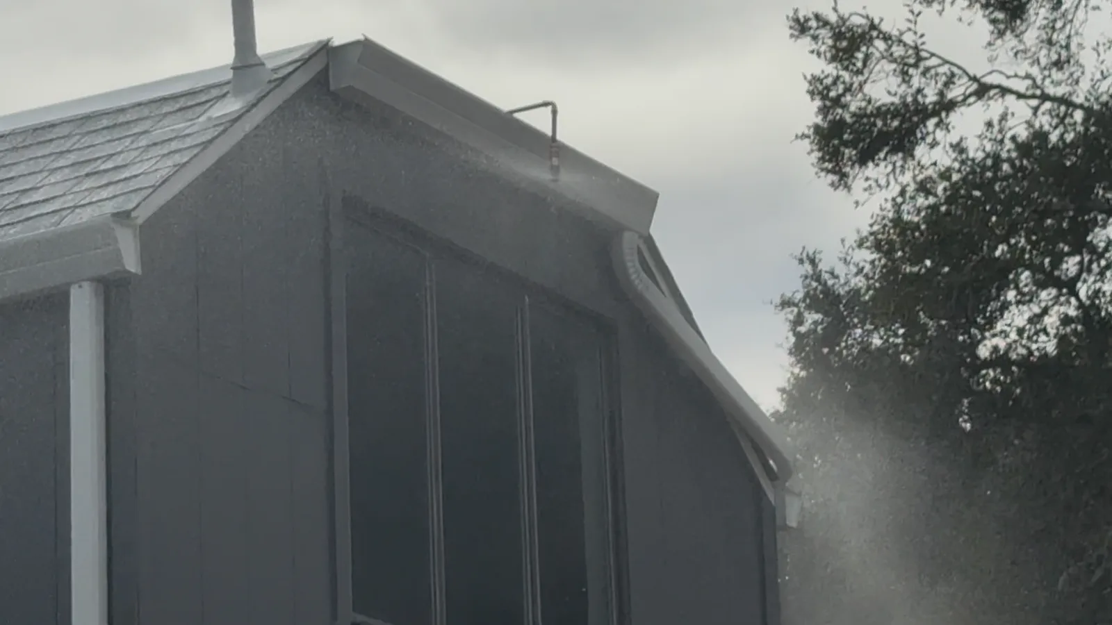 Eave sprinkler nozzle misting the gable and siding of a gray home