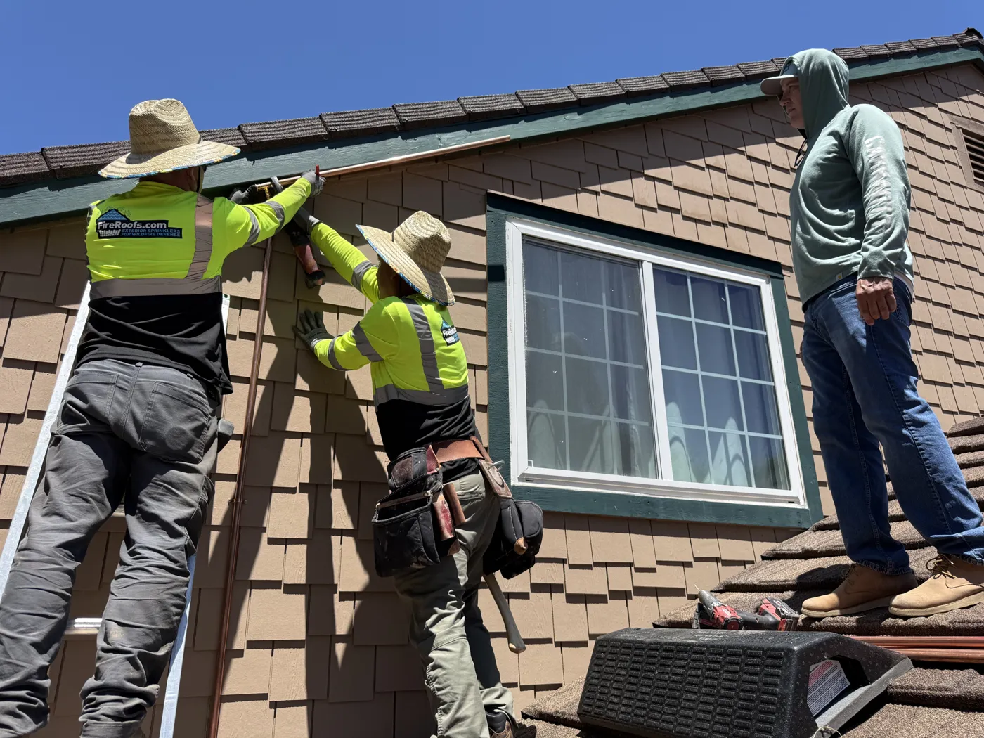 FireRoofs Vetted Installers fastening a copper sprinkler line along the eave of a shingle-sided home