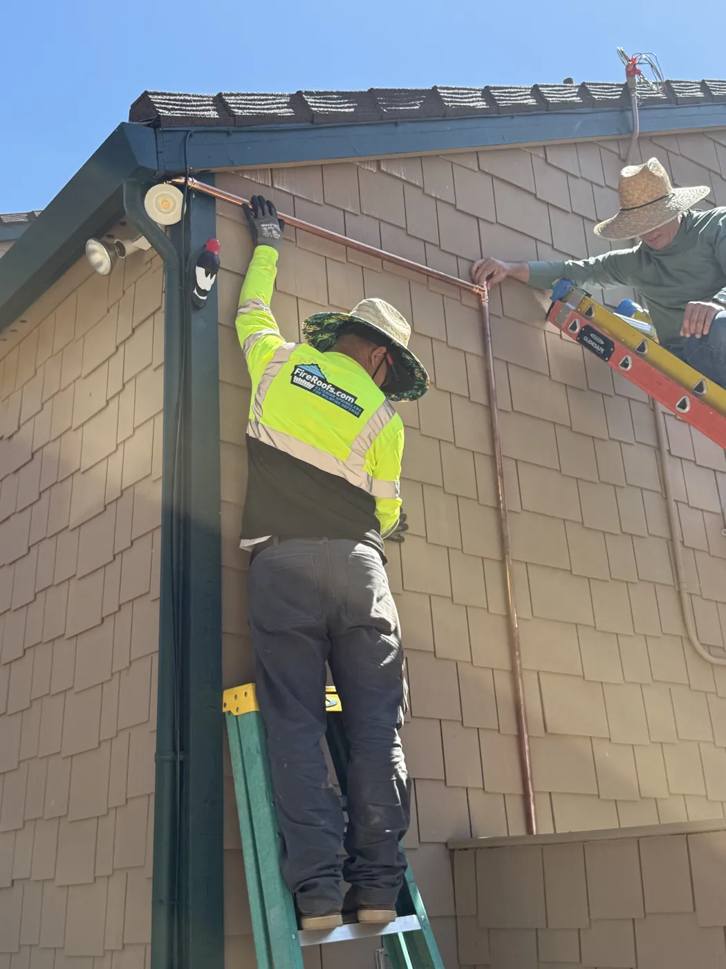 FireRoofs Vetted Installer on a ladder setting a copper riser at the corner eave of a home