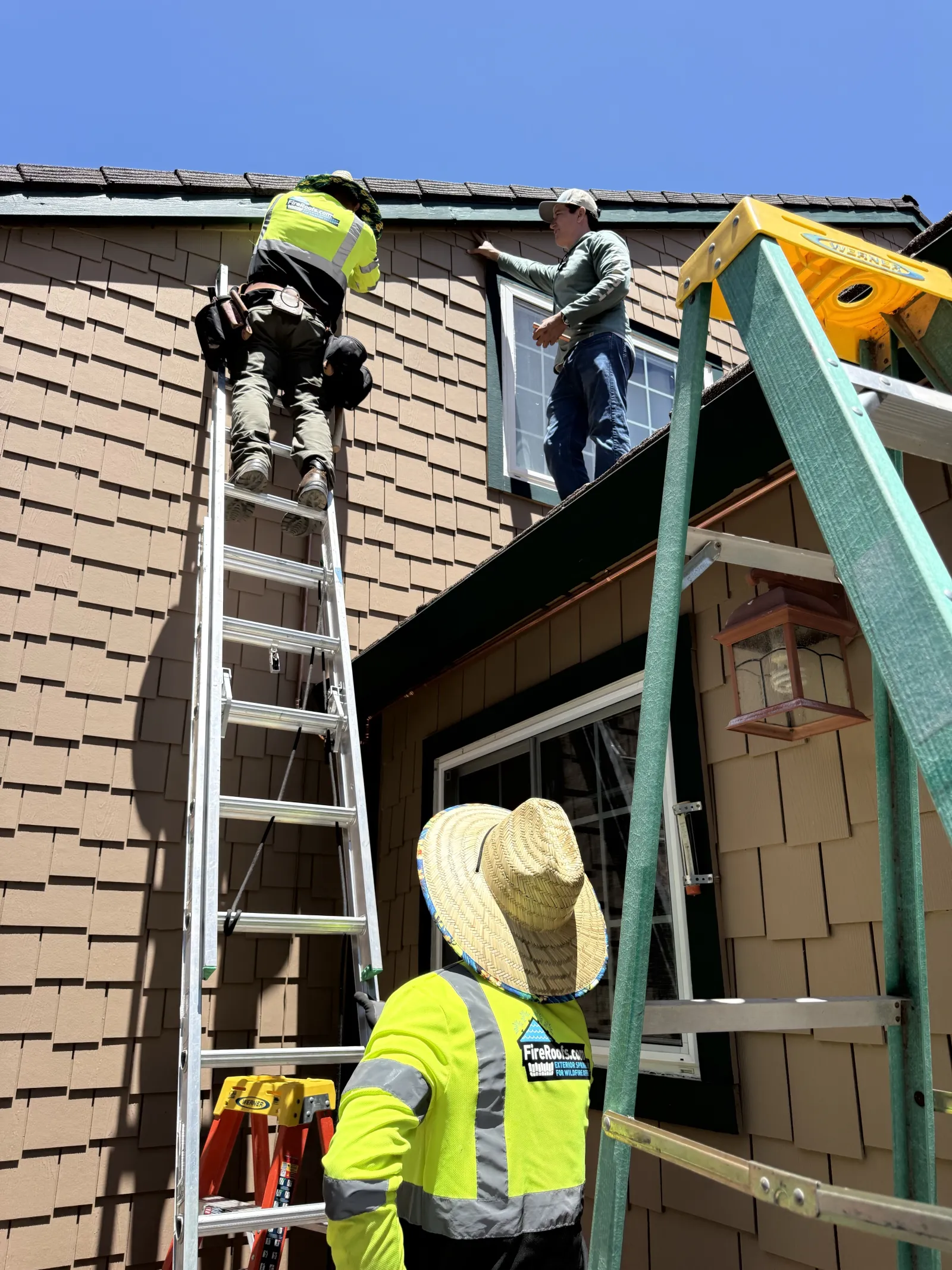 FireRoofs crew in high-visibility vests working from ladders to install an exterior wildfire sprinkler system along the roofline of a Bay Area home