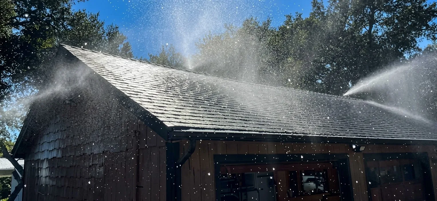 Roof sprinklers spraying water across a shingle roof on a wood-sided garage