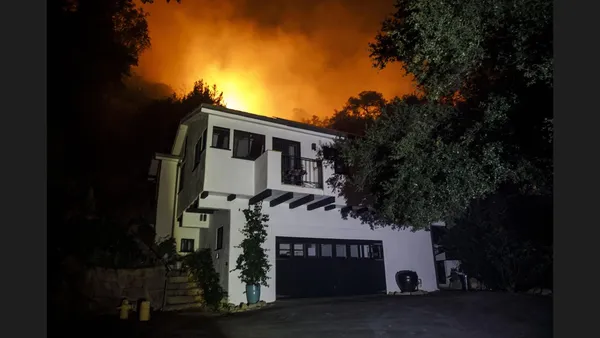 Wildfire approaching a WUI hillside community showing ember attack and radiant heat threat to residential structures.